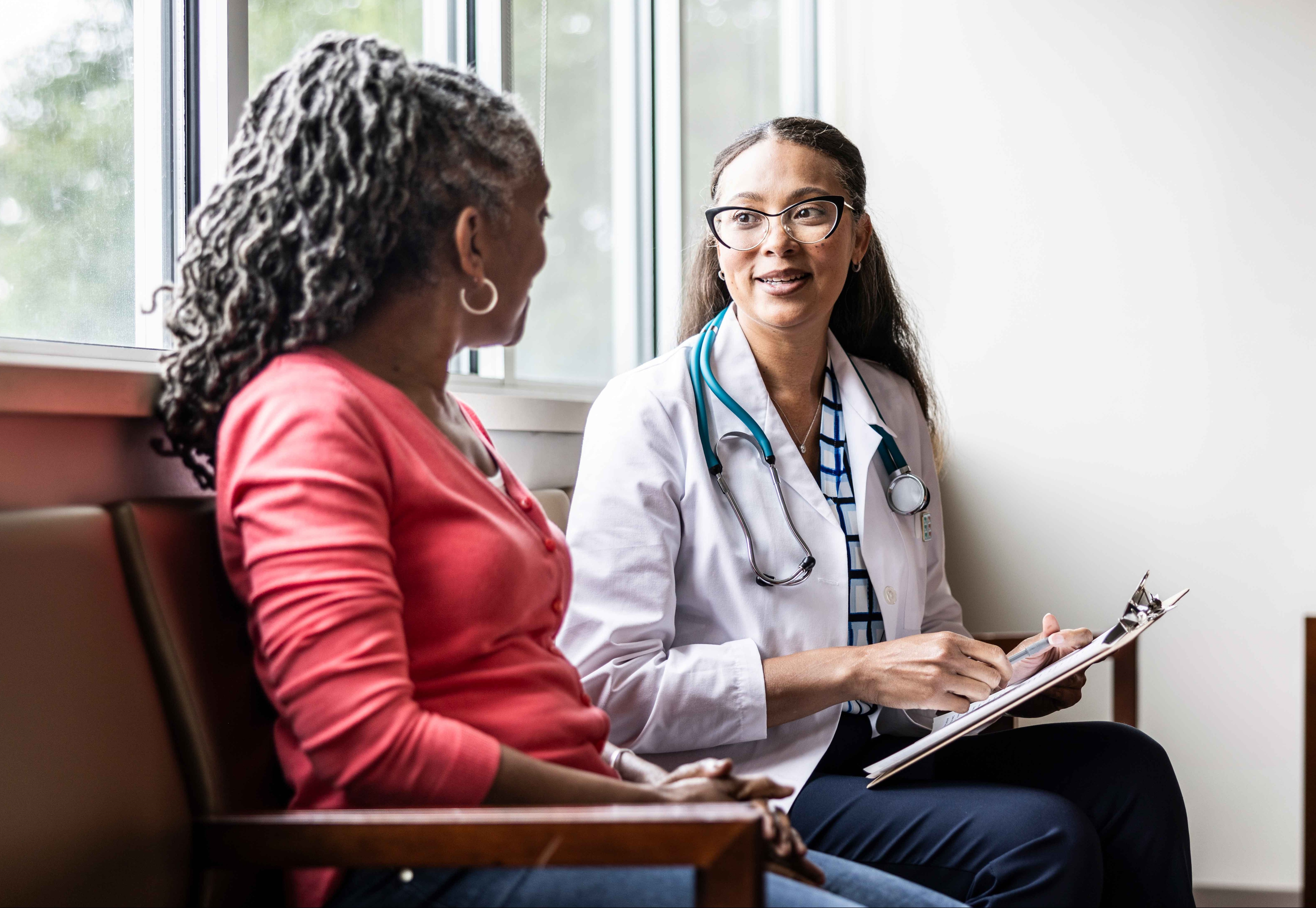 Photo of a young African-American doctor discussing COVID-19 signs and symptoms with an older African-American woman.